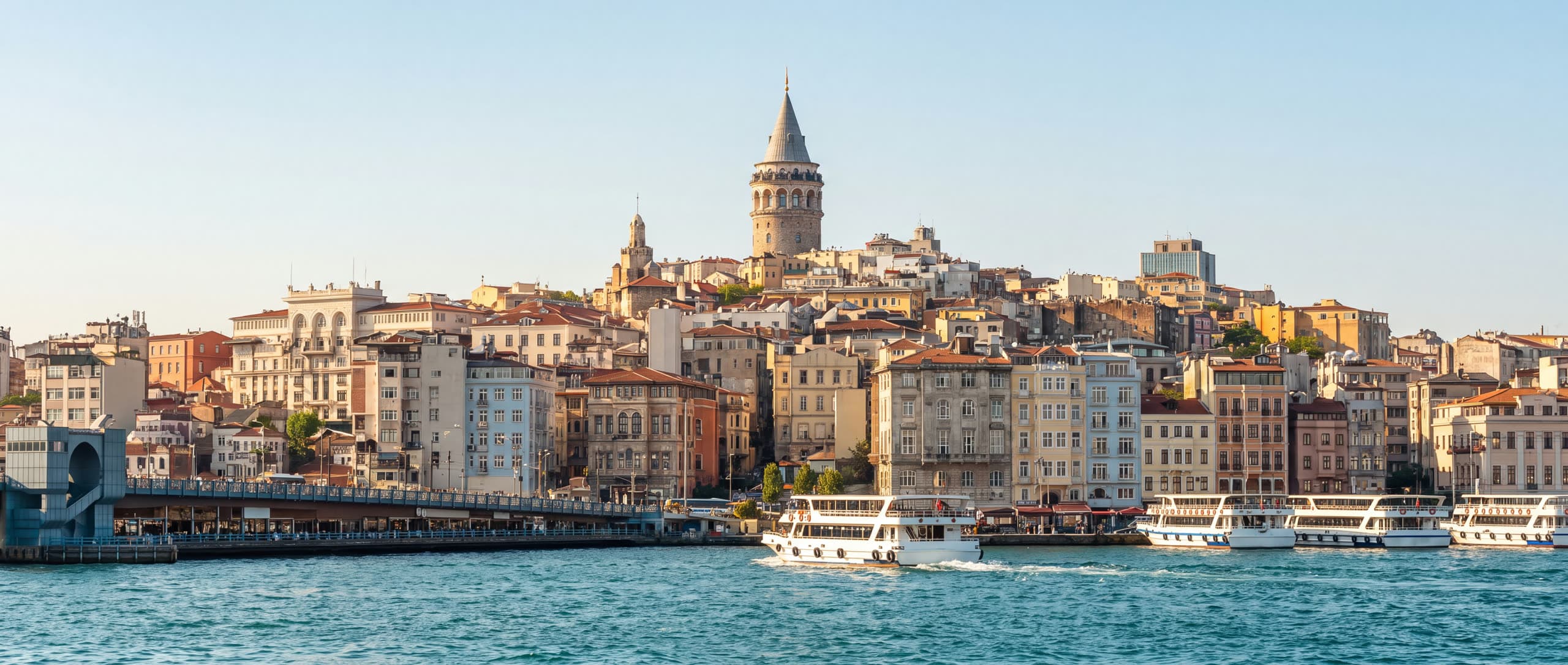 Daytime panorama of Istanbul's Golden Horn, with the Galata Tower rising above the waterfront, ferries crossing the strait, and the Galata Bridge in the distance